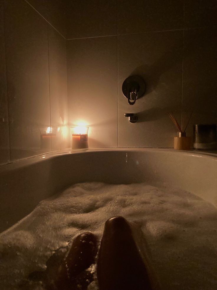 a person laying in a bathtub with soap on the floor and candles lit up behind them