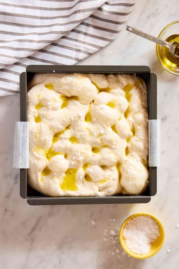 an uncooked pastry in a baking pan next to a glass of olive oil