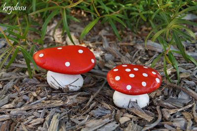 two small red and white mushrooms sitting on top of the ground next to some grass