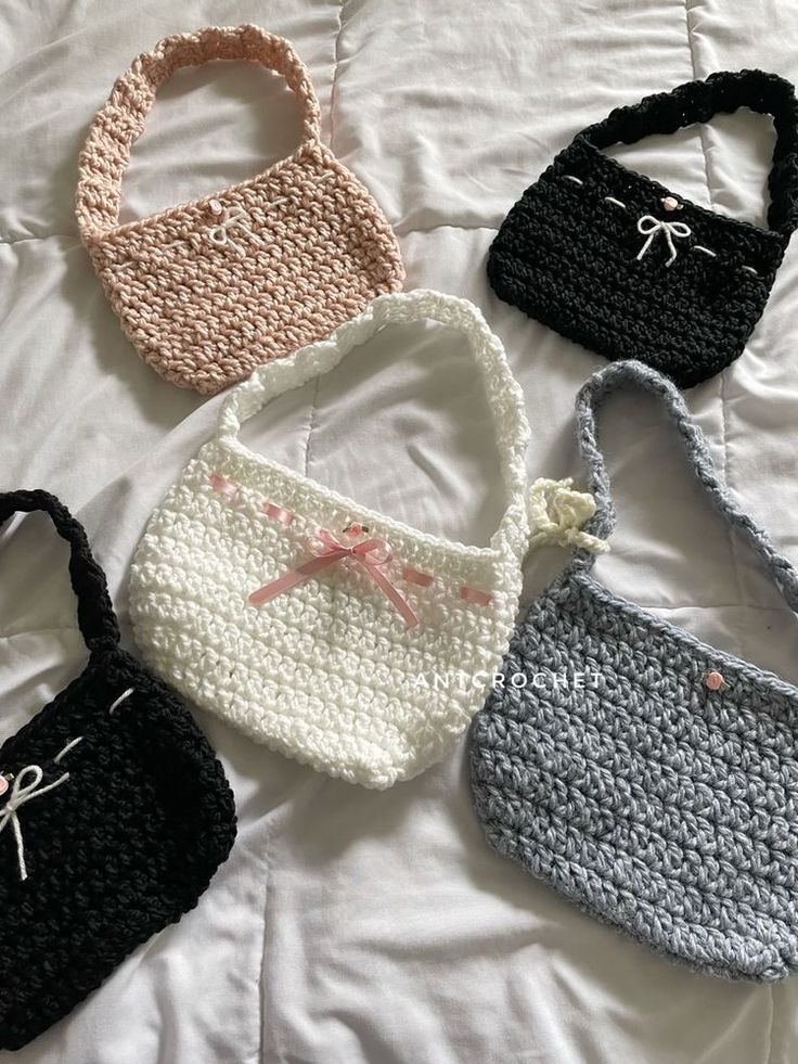 four crocheted purses sitting on top of a white bed next to each other