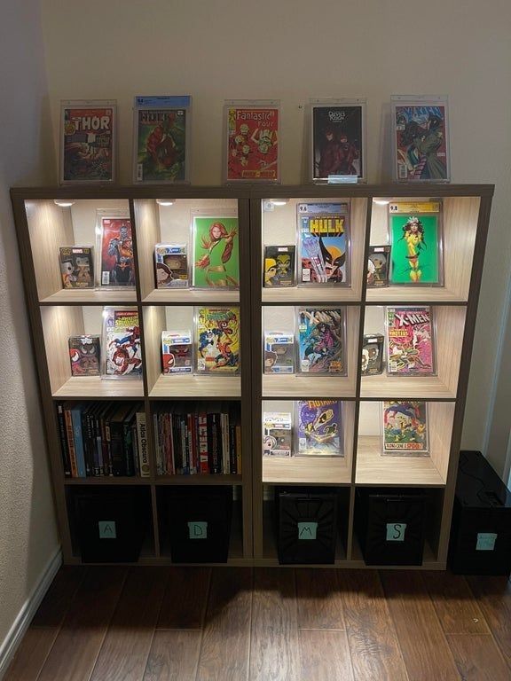 a book shelf filled with comic books on top of wooden floor next to a wall