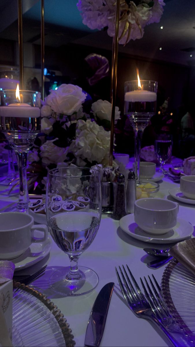 the table is set with white dishes and silverware, lit by candles in the background