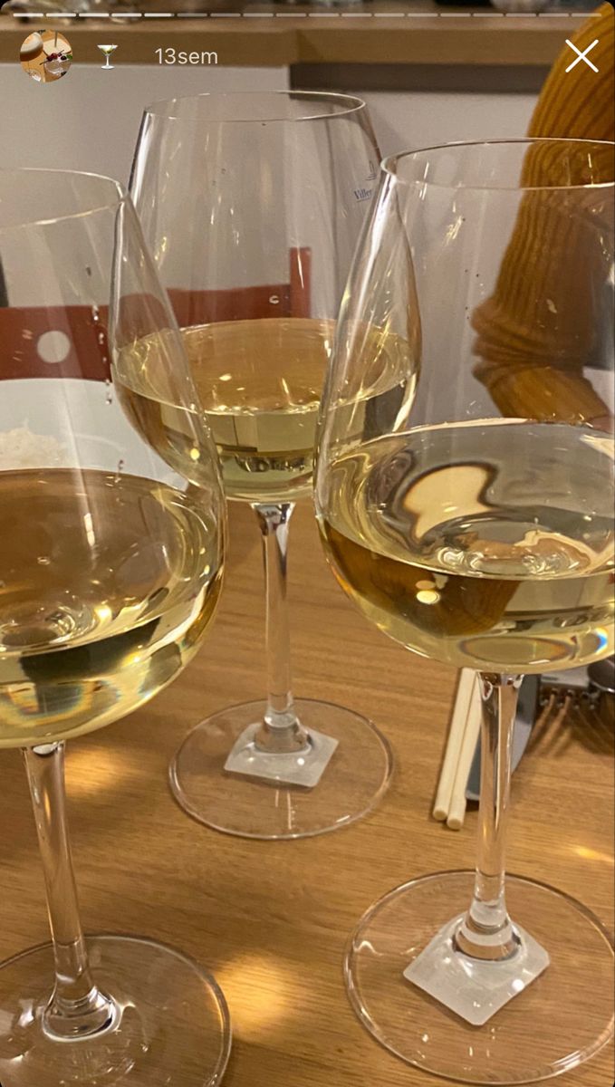 three wine glasses sitting on top of a wooden table next to each other with white wine in them