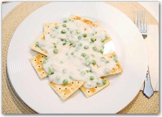 a white plate topped with nachos covered in cheese and green peas next to a fork