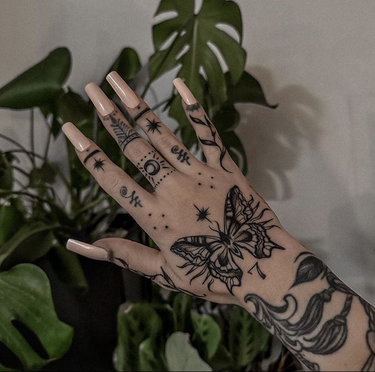 a person's hand with tattoos on it next to a potted green plant