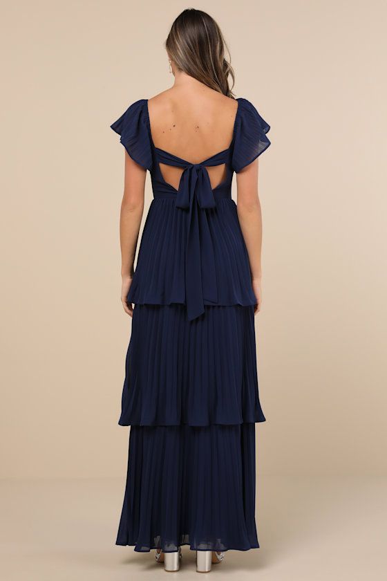 Everyone will instantly notice your sensational sense of style when you strut in wearing the Lulus Notorious Charm Navy Blue Pleated Flutter Sleeve Maxi Dress! Airy, pleated woven chiffon shapes this gorgeous dress that features a lightly gathered bodice with a sweetheart neckline and long sashes that secure atop an otherwise open back, framed by fluttery short sleeves (with elastic at the shoulders). The high, fitted waist tops a flowy, tiered A-line skirt that cascades down to a sweeping maxi hem. Hidden back zipper/clasp. Fit: This garment fits true to size. Length: Floor length. Size medium measures 53.75" from shoulder to hem. Bust: Great for any cup size. Waist: Fitted - very fitted at natural waist. Hip: Not Fitted - room for hips. Undergarments: May be worn with an adhesive bra, pe