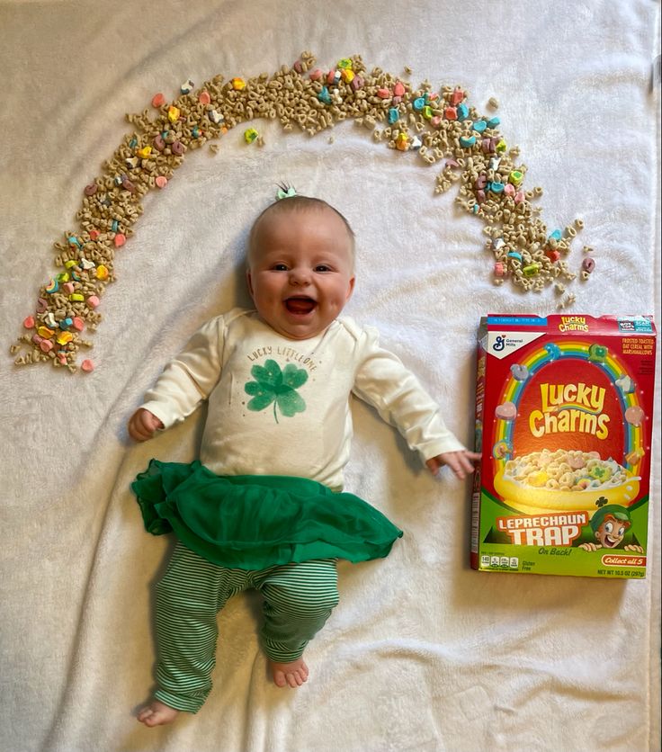 a baby laying on top of a bed next to a box of lucky charms