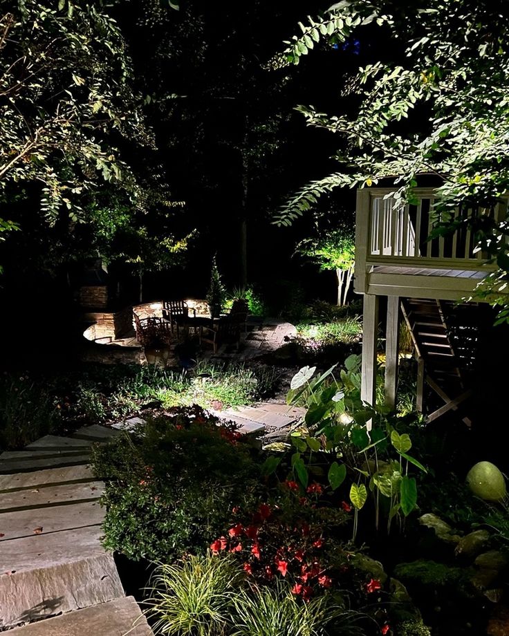 a wooden walkway in the middle of a garden at night with lights shining on it