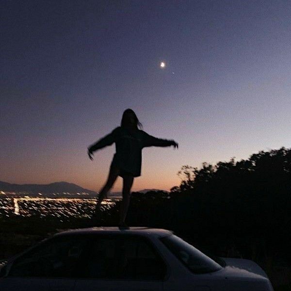 a person standing on top of a car in the dark with their arms spread out