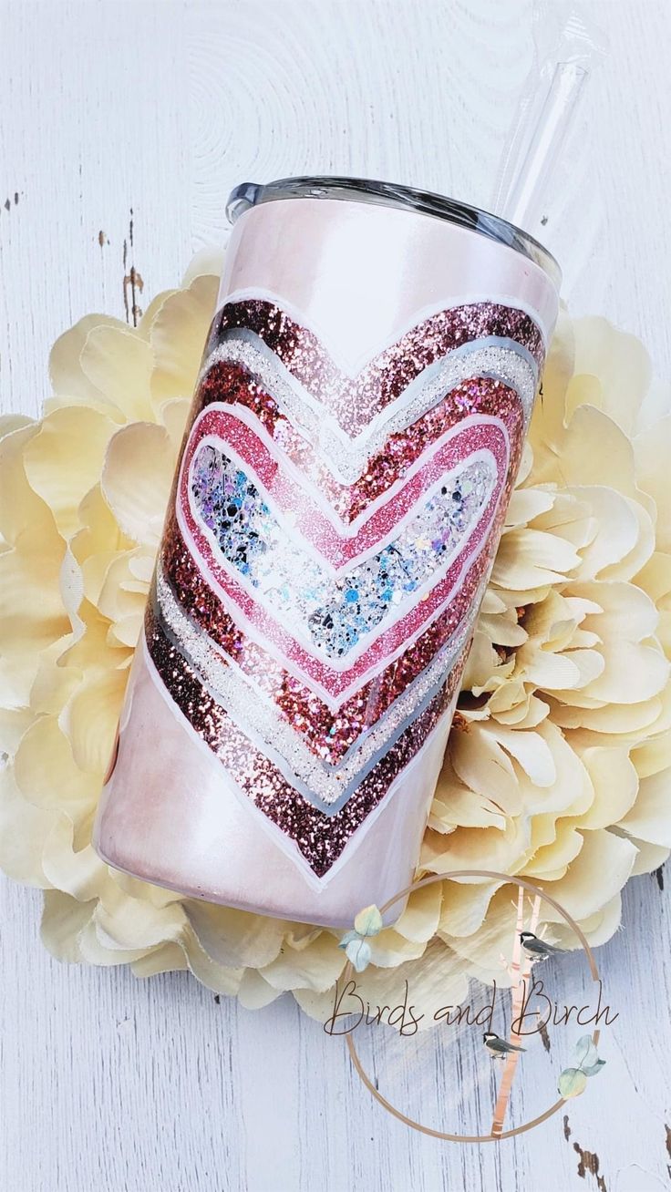 a pink glitter tumbler with a heart painted on the side and flowers around it