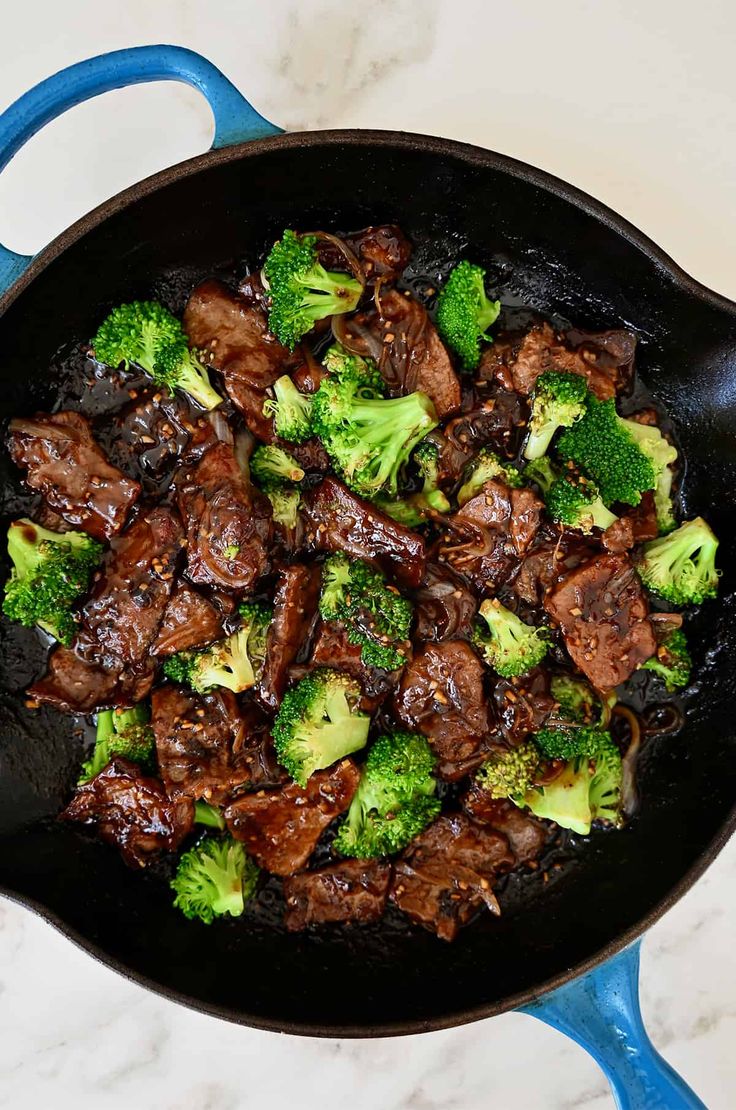 beef and broccoli in a skillet on a marble counter top with blue spatula