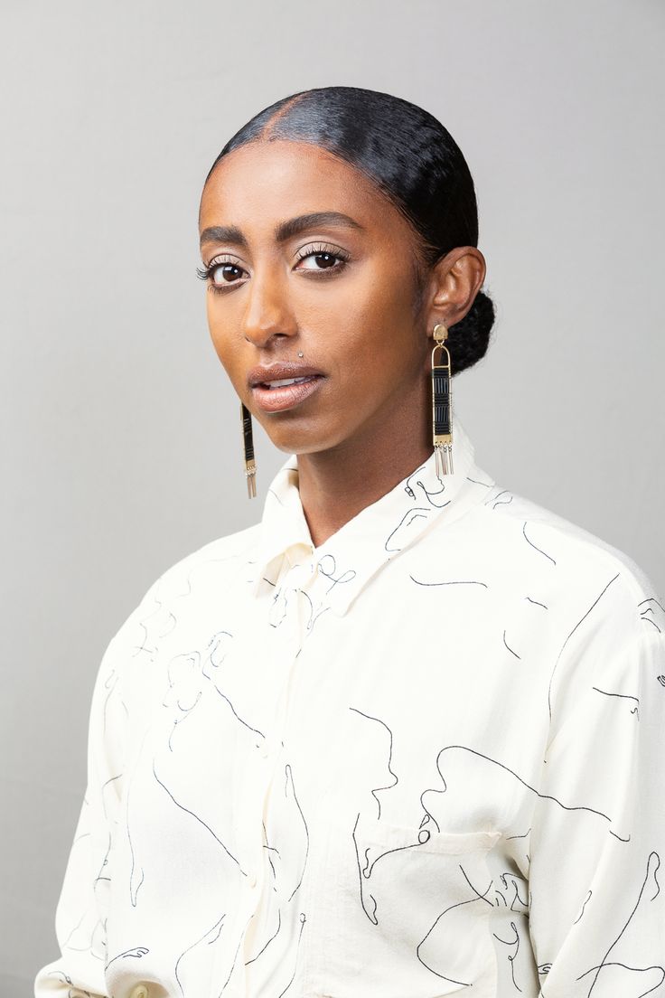 a woman with black hair wearing earrings and a white shirt