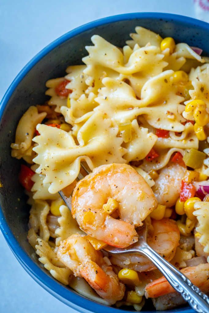 a blue bowl filled with pasta and shrimp next to a silver serving spoon on top of a table