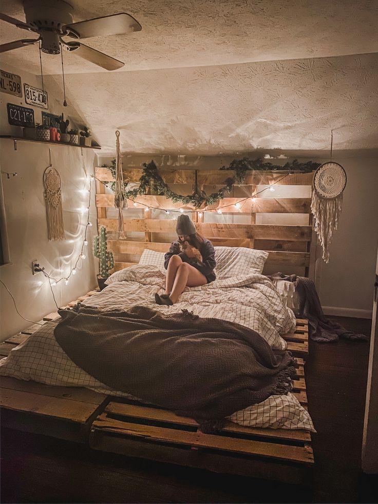 a woman sitting on top of a bed in a room with wooden pallets and lights