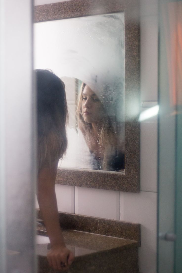 a woman standing in front of a mirror with her reflection on the bathroom counter top