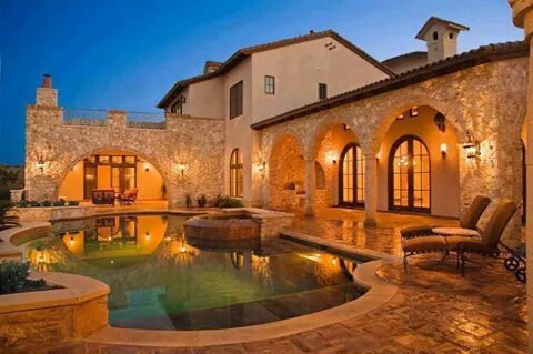 an outdoor swimming pool surrounded by stone walls and arches with lights on the side of it