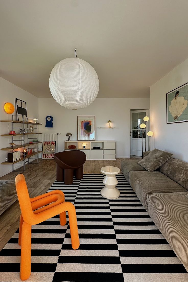 a living room with black and white striped rugs on the floor, two orange chairs sitting in front of a gray couch