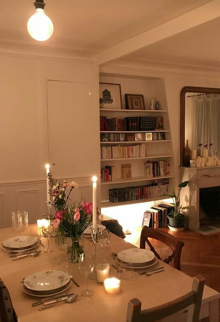 a dining room table is set with plates and candles in front of bookshelves