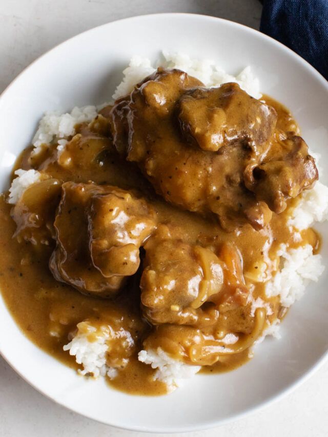 a white plate topped with meat and gravy covered in gravy on top of rice