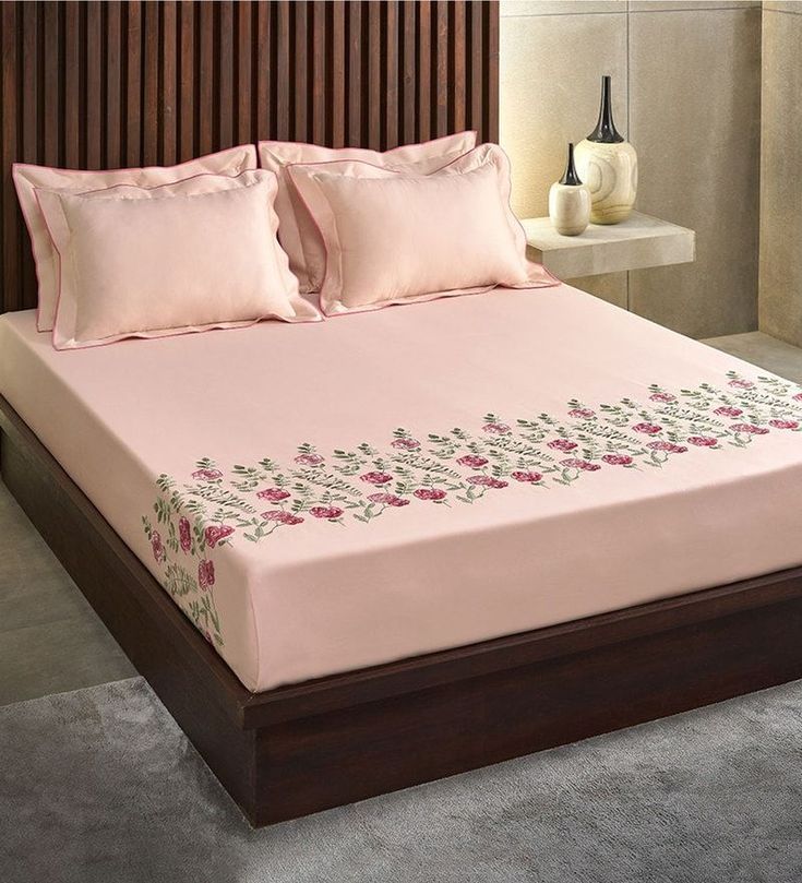 a bed with pink sheets and pillows on top of it in a room next to a vase