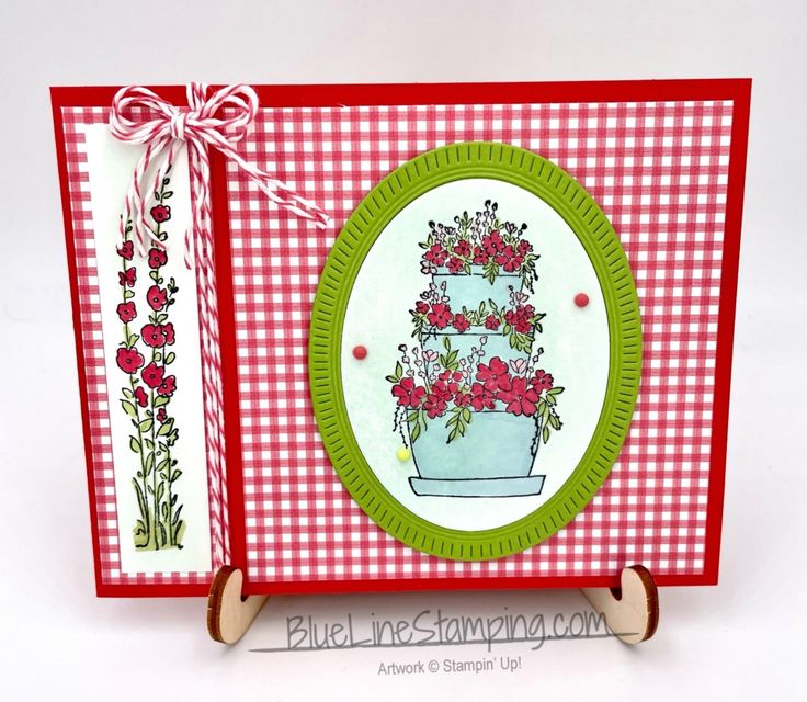 a handmade card with red flowers and green trimmings on the front, sitting on a wooden stand