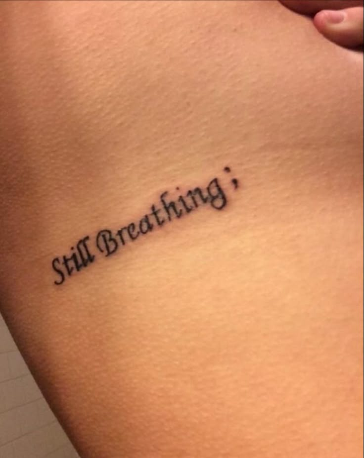 a woman's stomach with the words still breathing tattooed on her lower side ribcage