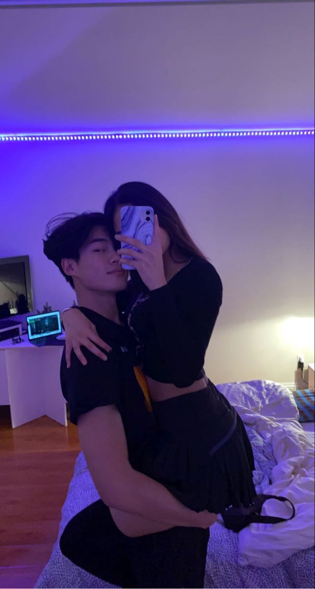 a man and woman taking a selfie in the bedroom with blue lights on the ceiling