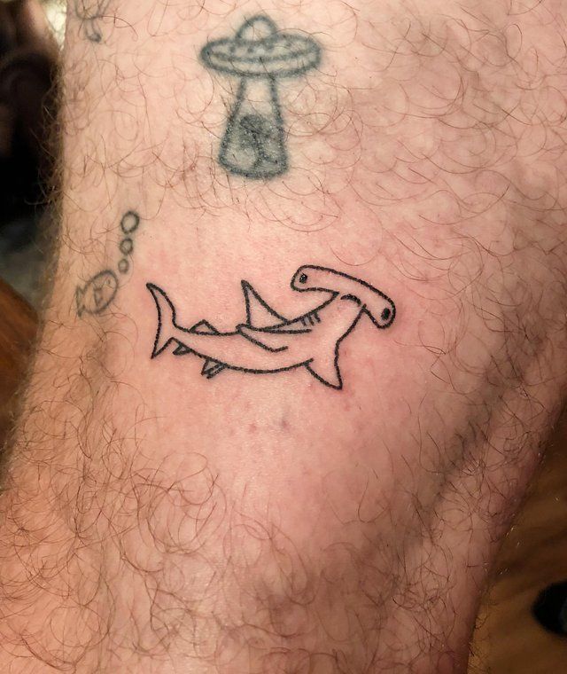 a man with a tattoo on his leg has a shark and an alien ship in the background