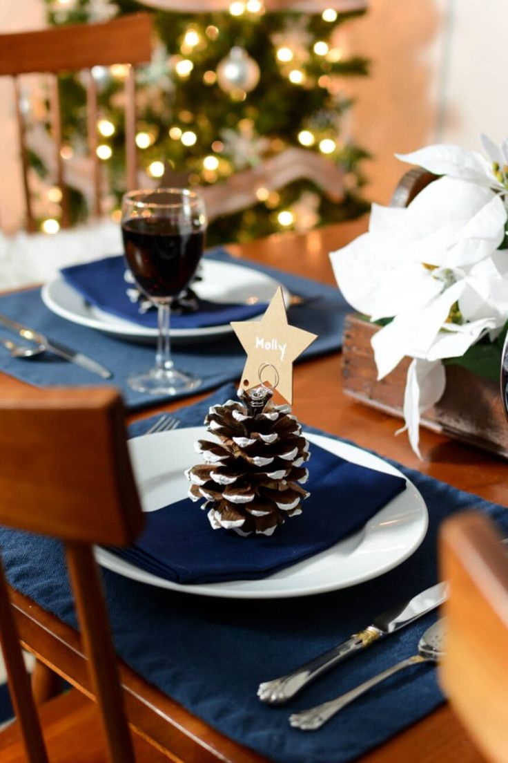 a dining room table set for christmas with blue and white place settings, silverware, and a pine cone centerpiece