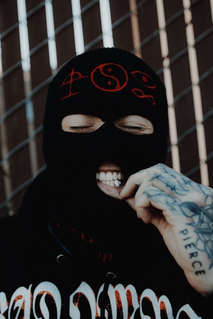 a man wearing a black mask and holding his hand up to his face with tattoos on it