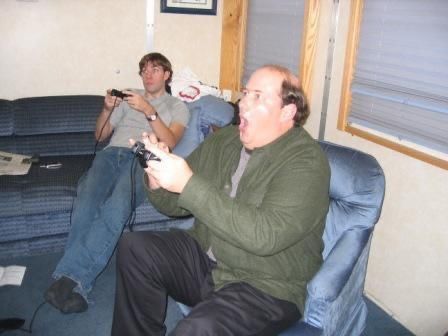 two men sitting on couches playing video games with remote controllers in their hands while another man watches