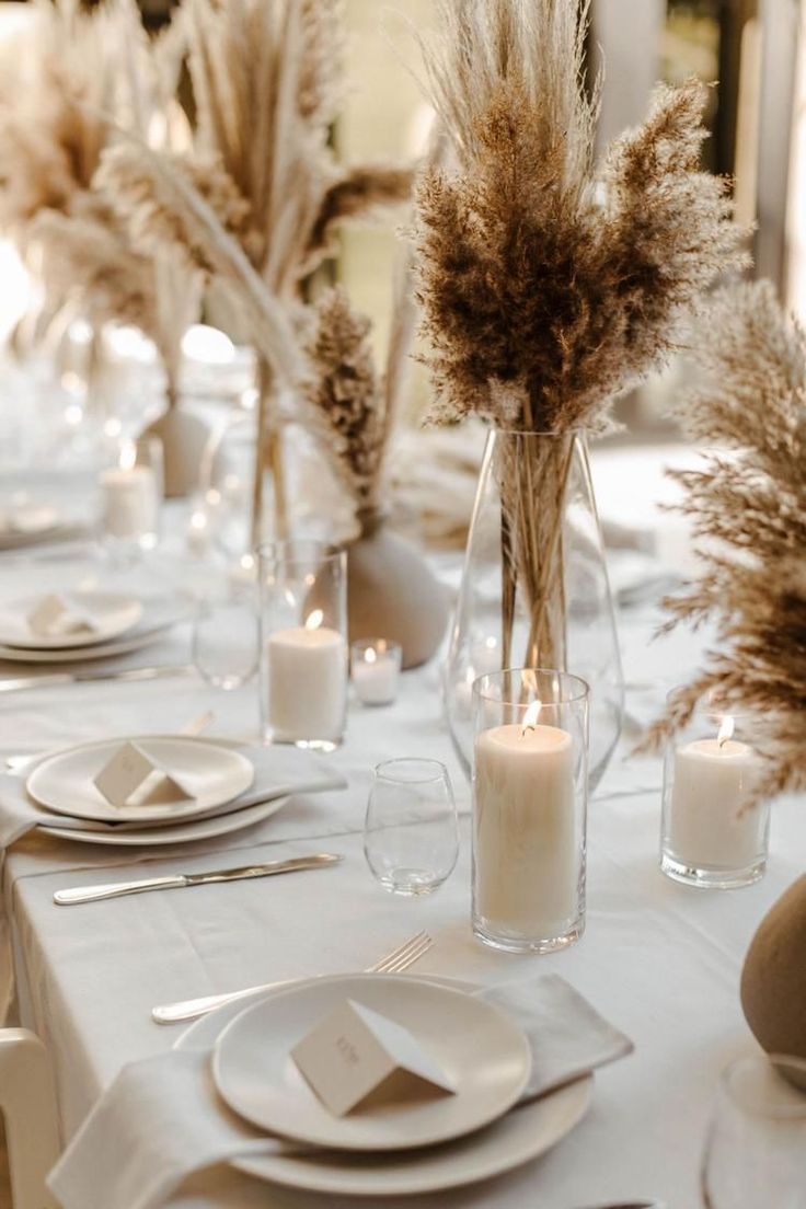 the table is set with white plates, silverware and tall vases filled with flowers