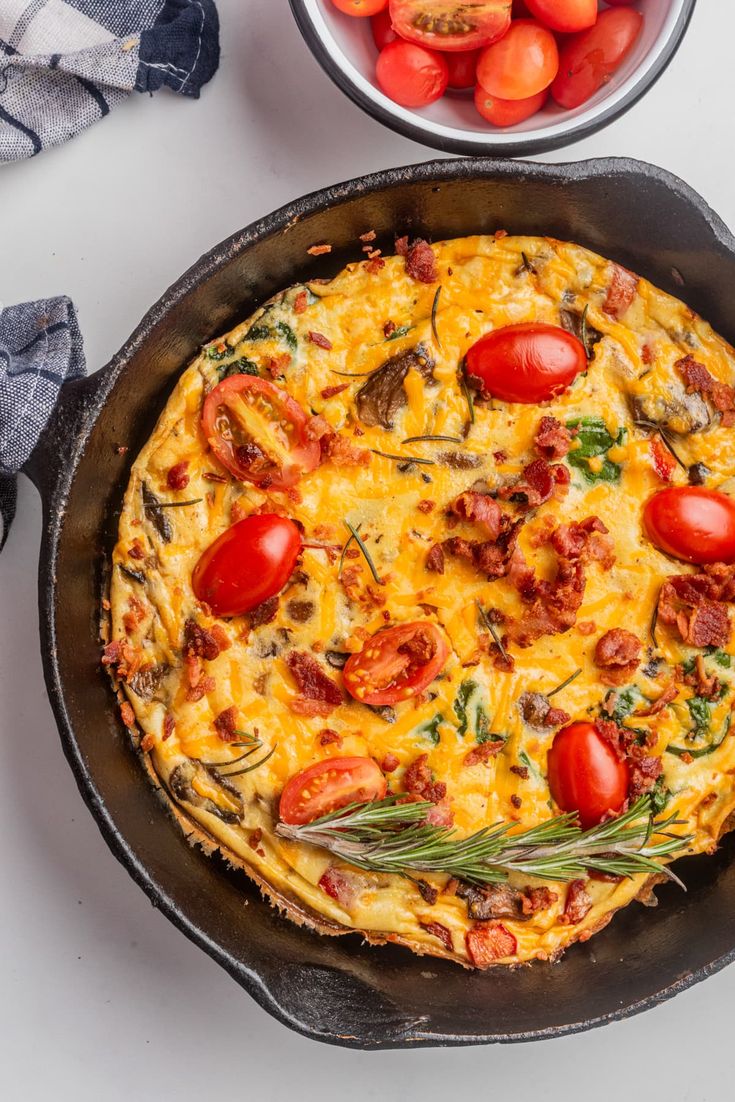 an omelet with tomatoes and herbs in a cast iron skillet next to a bowl of cherry tomatoes