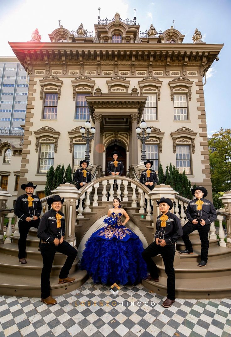 a woman in a blue dress standing on the steps of a building with other people behind her