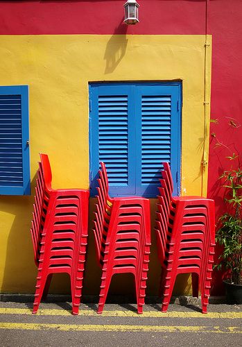 four red chairs sitting in front of a yellow building with blue shutters and windows