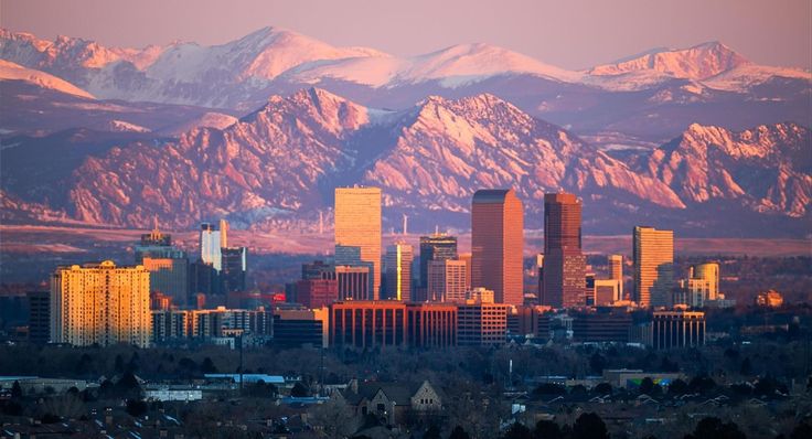 the city is surrounded by mountains and snow capped peaks in the distance, as seen from across the valley