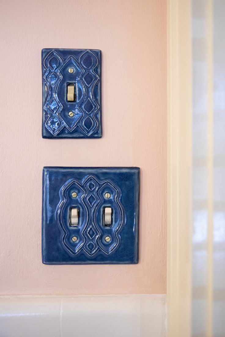 two blue light switch plates mounted to the side of a pink wall with white trim