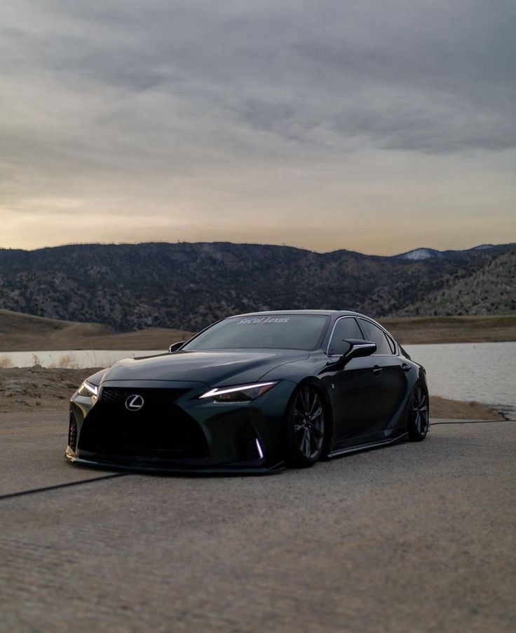 a black sports car driving down a road next to a body of water with mountains in the background