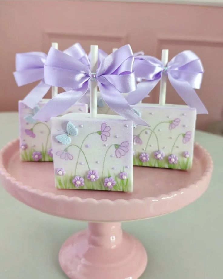 three small boxes with purple bows on them sitting on a cake plate in front of a pink wall