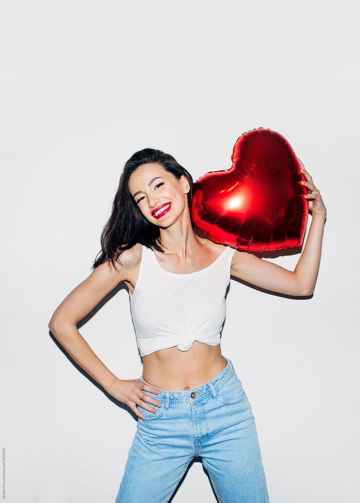 a woman holding a heart shaped balloon in front of her face and posing for the camera