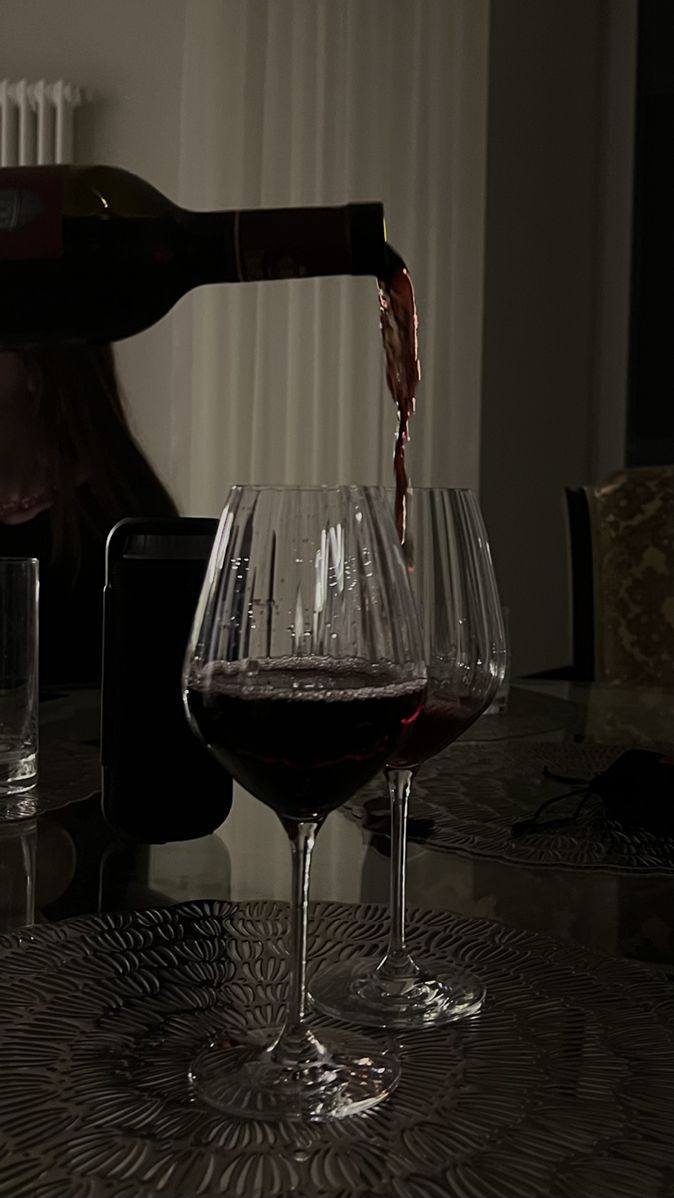 a person pouring wine into two glasses on a table