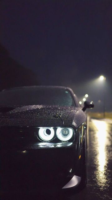 a black car with its eyes glowing in the rain at night, next to a street light