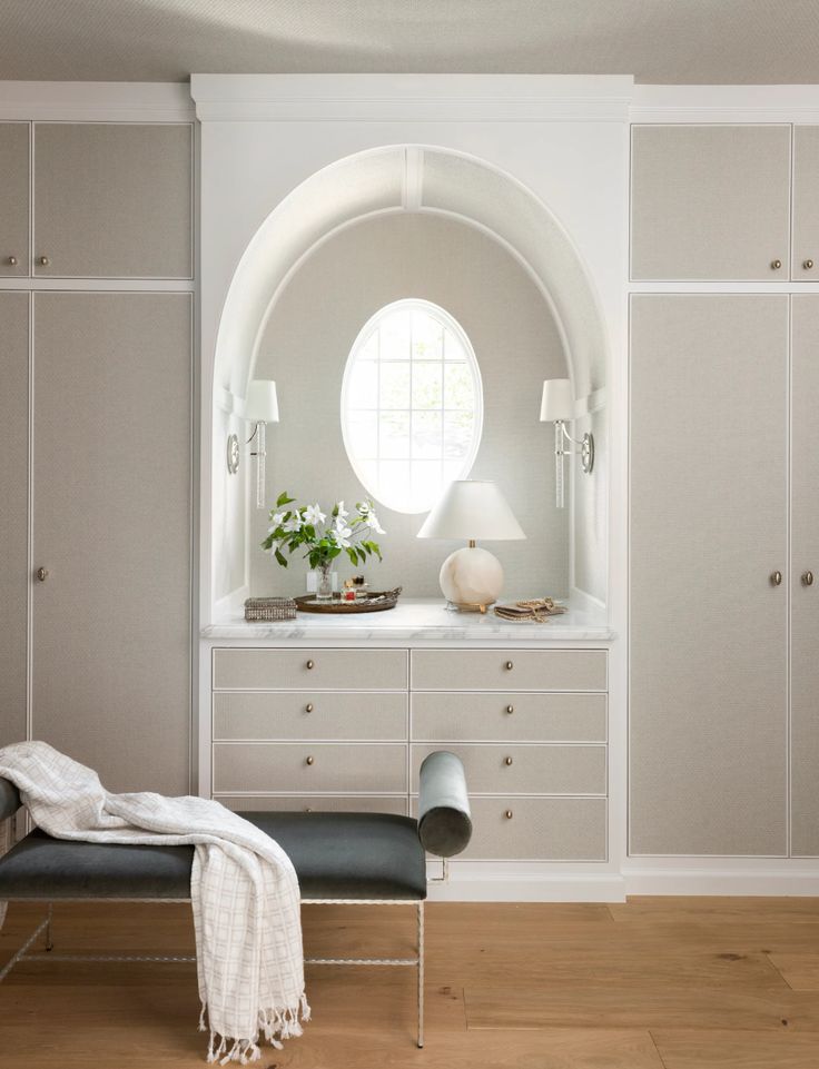 a bedroom with white furniture and a round window in the wall behind it is a bench