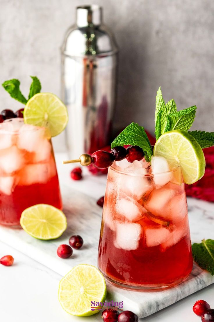 two glasses filled with cranberry lemonade and limes on a marble tray