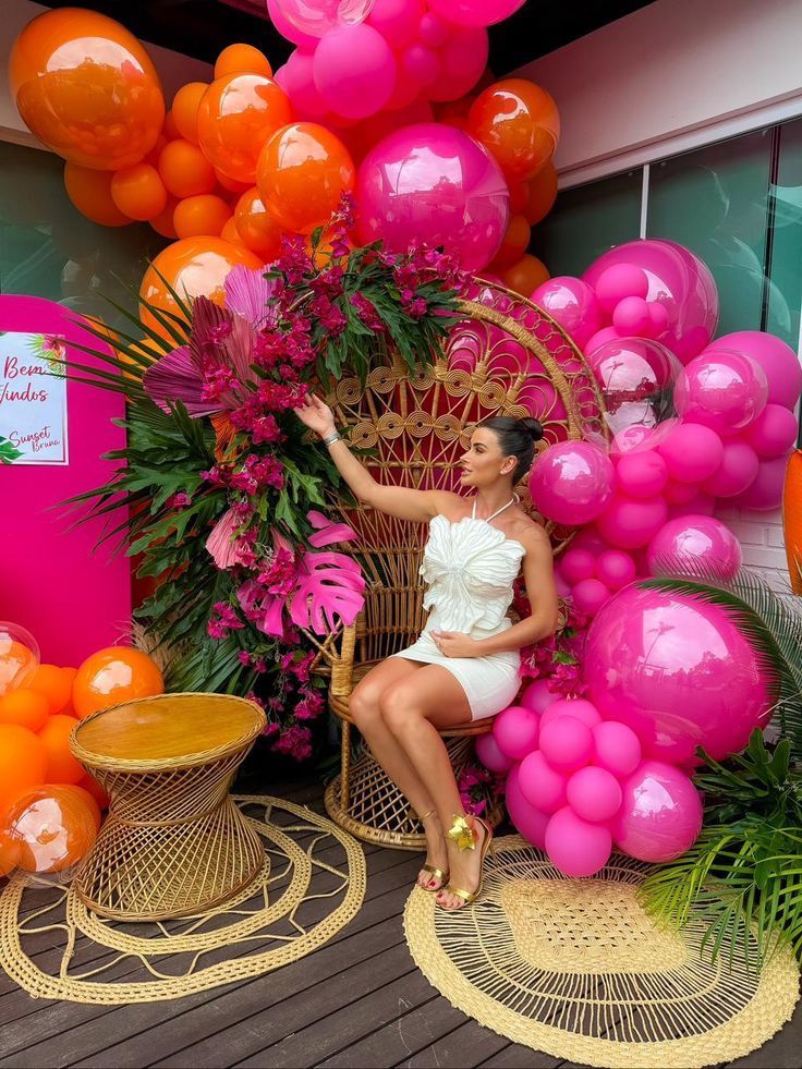 a woman sitting on a wicker chair surrounded by pink and orange balloons in the background