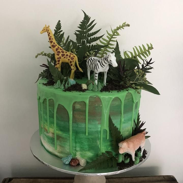 a cake decorated with green icing and jungle animals is on a table in front of a white wall