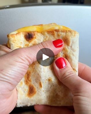 a hand holding a piece of bread with cheese on it and a red manicure