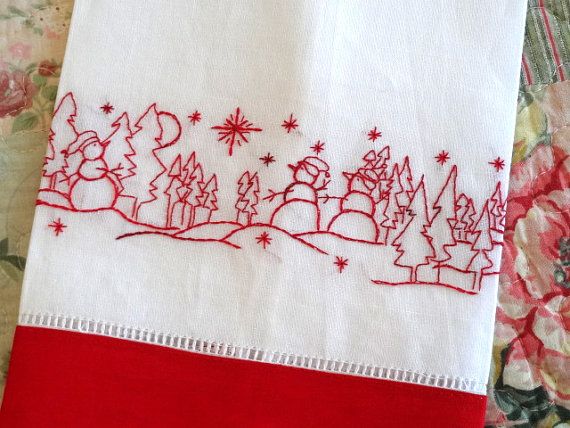 a red and white table cloth with embroidered christmas scene on it, sitting on a quilted surface