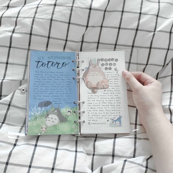 someone is holding an open book on top of a bed with white sheets and black checkered sheets