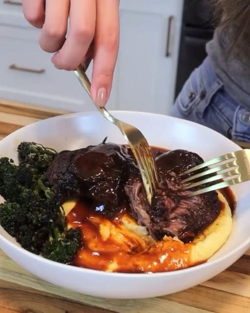 a person is cutting into some meat with broccoli on the side in a white bowl